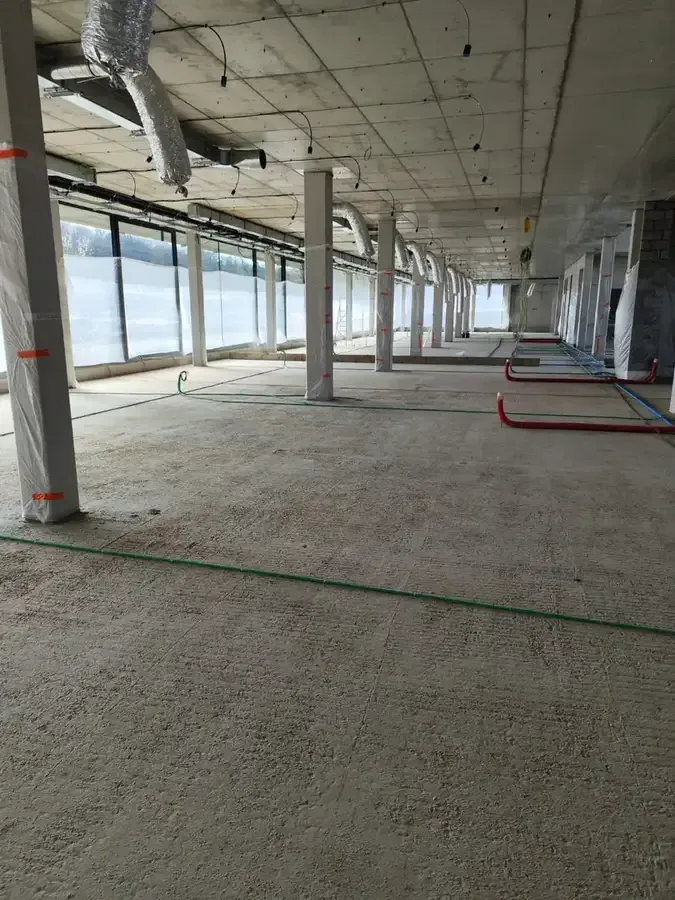 Immense plateau de bureaux en chantier, sol isolé à la mousse polyuréthane projetée, baies vitrées protégées par des bâches