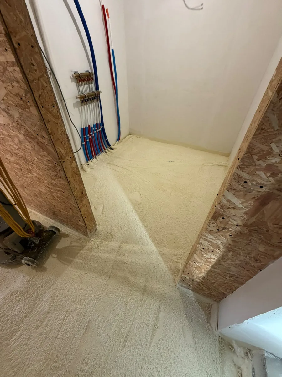 Sol d'une pièce en chantier isolé à la mousse polyuréthane projetée, nourrice de chauffage au mur